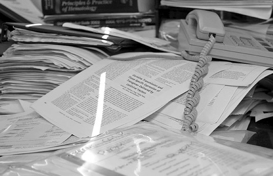 PAPERWORK A pile of paperwork on a desk, with an old style phone and a stream of light artistically highlighting the paper.