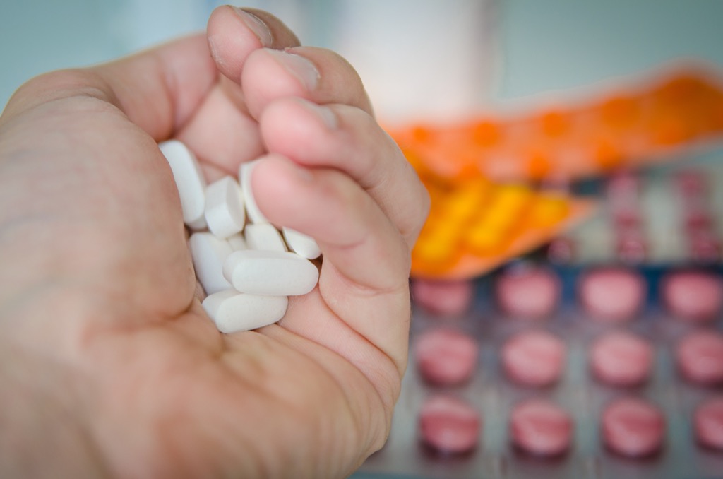 A hand holding a large pile of pills, in front of a background of pills